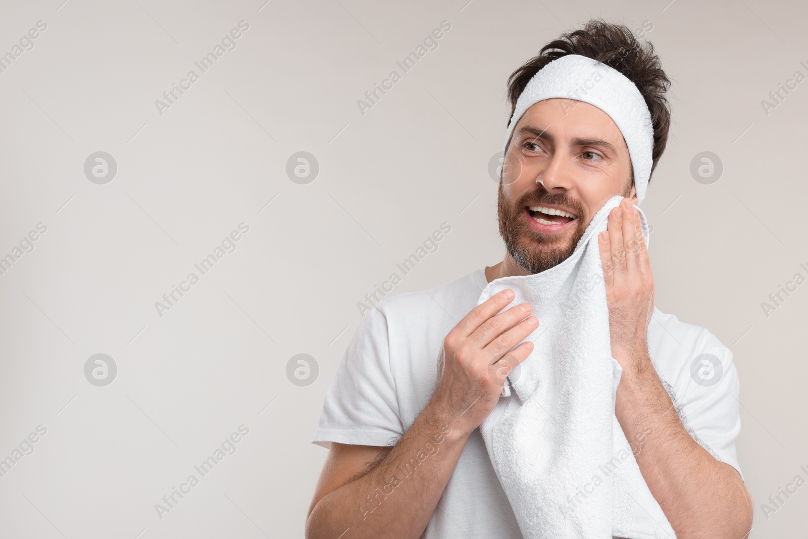 Photo of Washing face. Man with headband and towel on light grey background, space for text