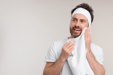 Photo of Washing face. Man with headband and towel on light grey background, space for text