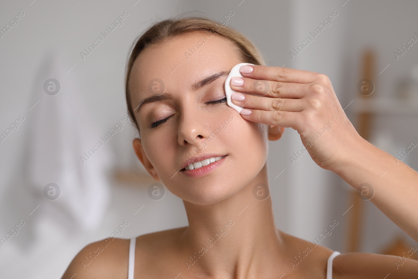 Photo of Smiling woman removing makeup with cotton pad indoors, closeup