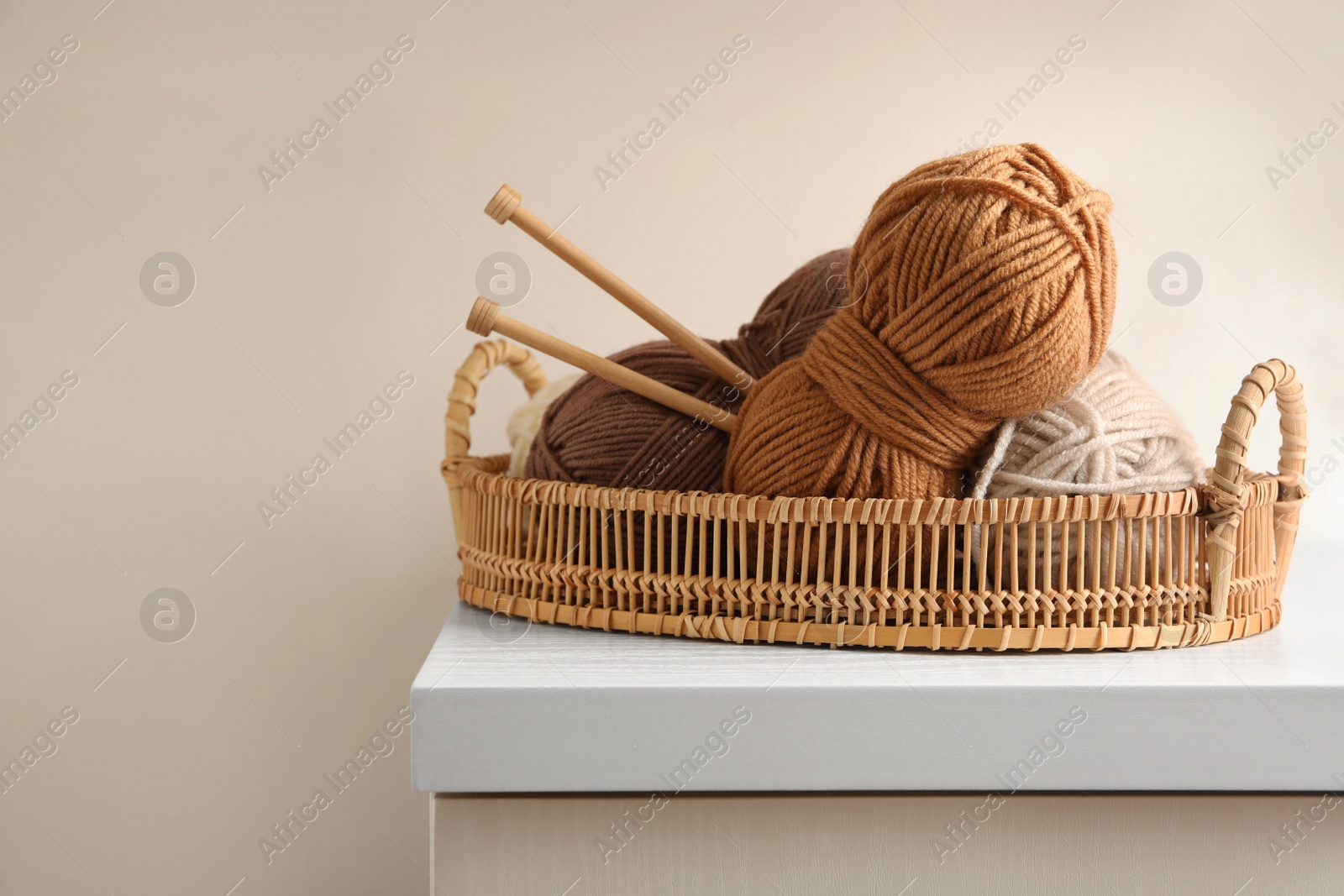 Photo of Woolen yarns and knitting needles in basket on white wooden table