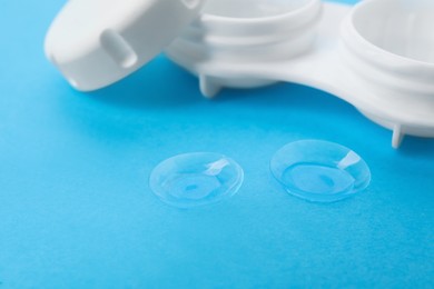 Contact lenses and case on light blue background, closeup