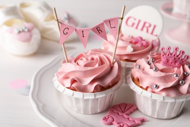 Photo of Delicious cupcakes with pink cream and toppers for baby shower on plate, closeup