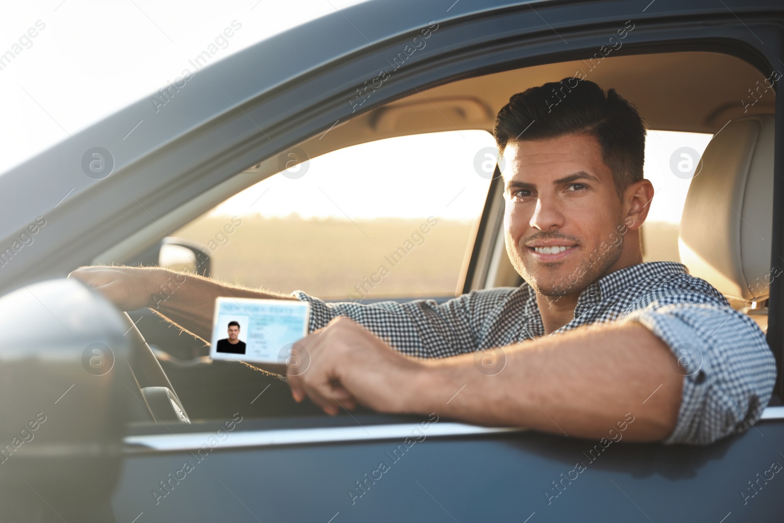 Photo of Happy man holding license while sitting in car outdoors. Driving school