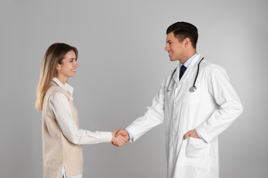 Photo of Doctor and patient shaking hands on light grey background