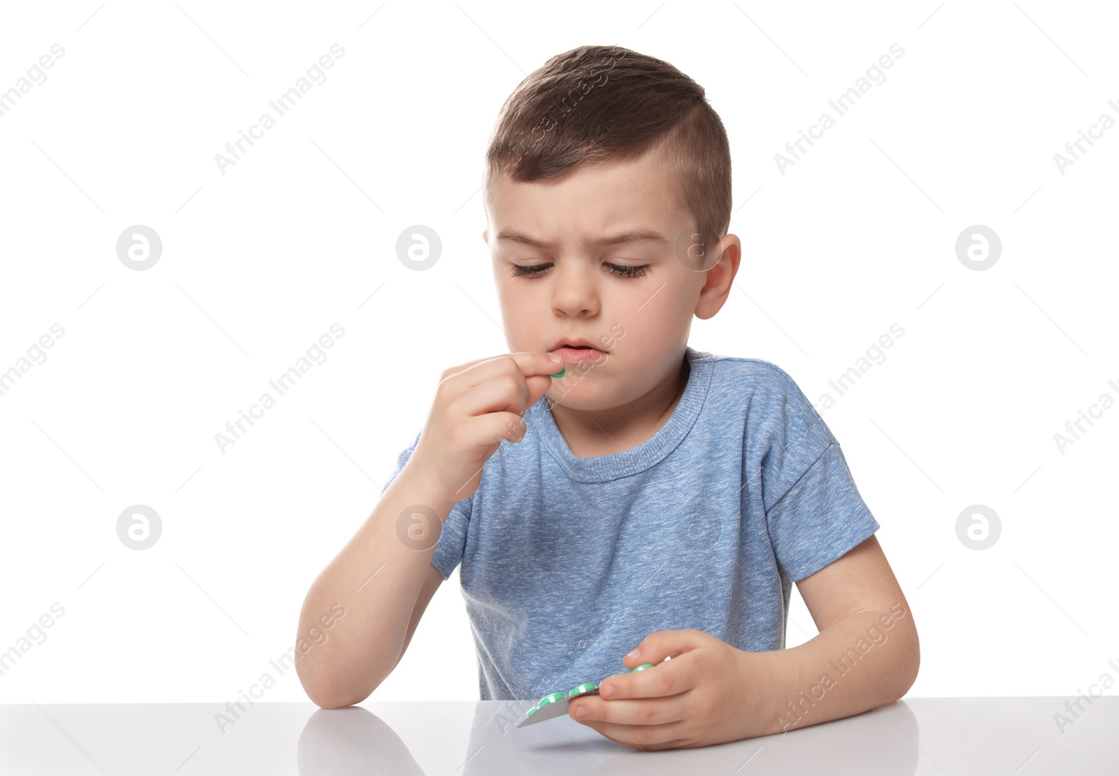 Photo of Little child taking pill on white background. Household danger