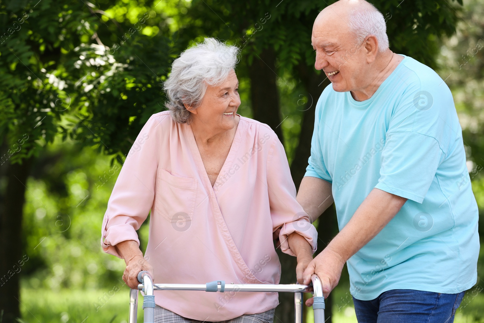 Photo of Elderly man helping his wife with walking frame outdoors