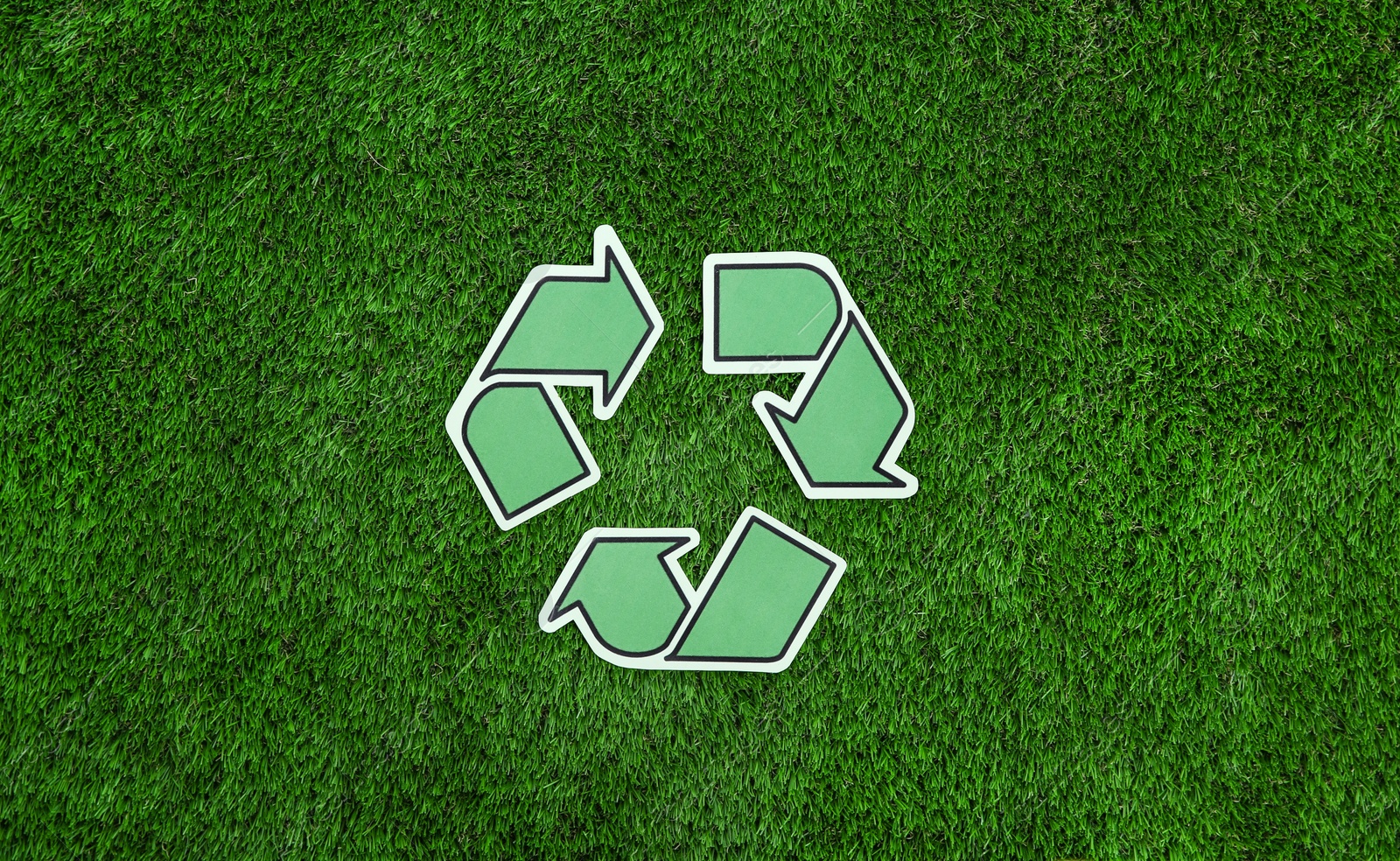 Photo of Paper recycling symbol on green grass, top view