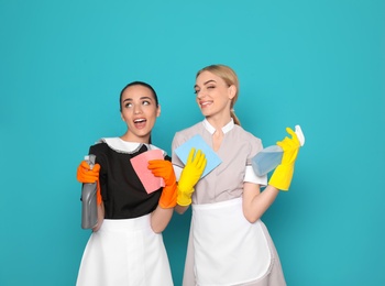 Young chambermaids with rags and detergents on color background