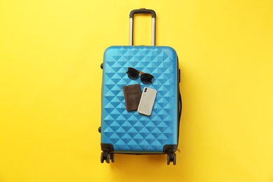 Stylish suitcase with sunglasses, smartphone and passport on color background, top view