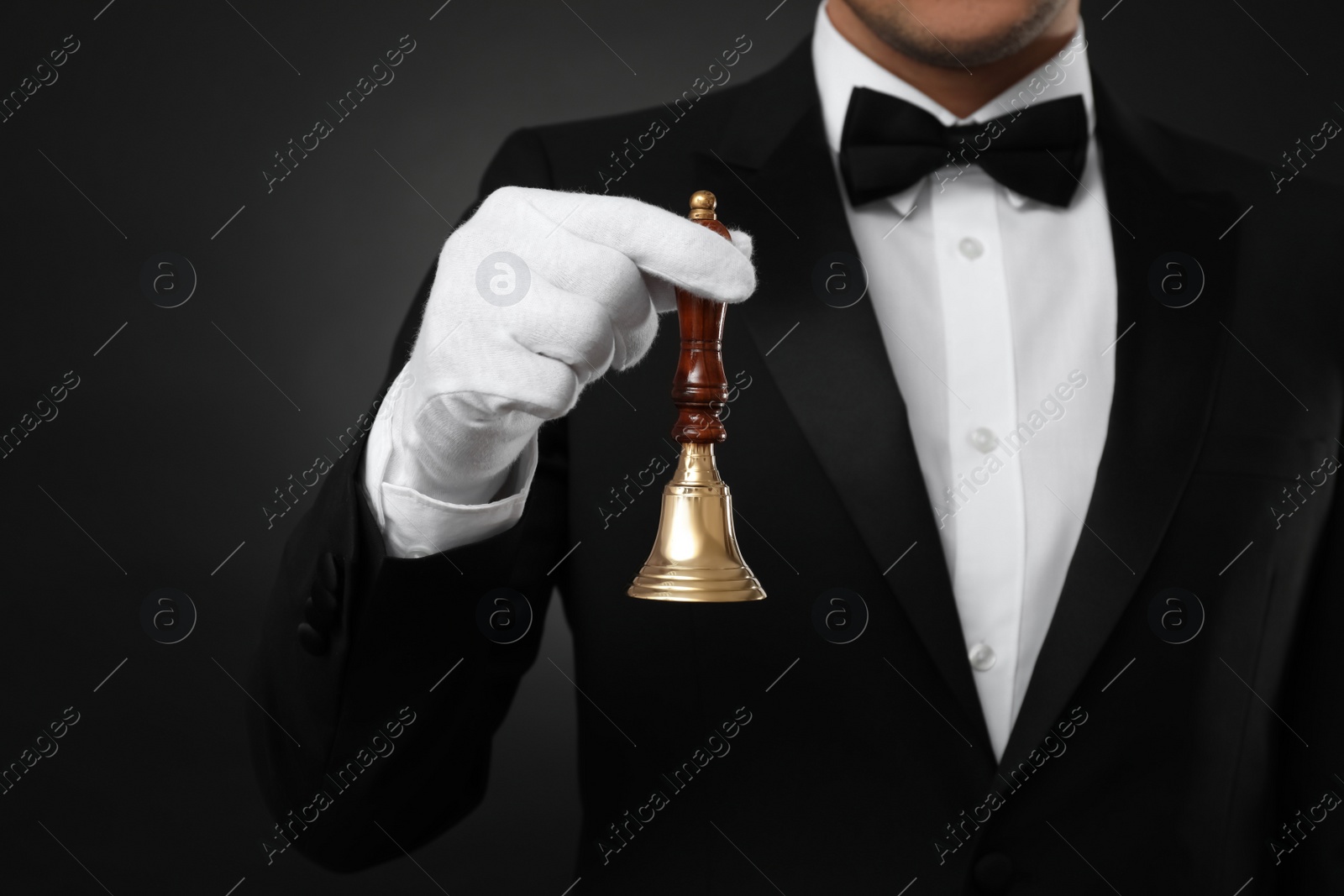 Photo of Butler holding hand bell on black background, closeup