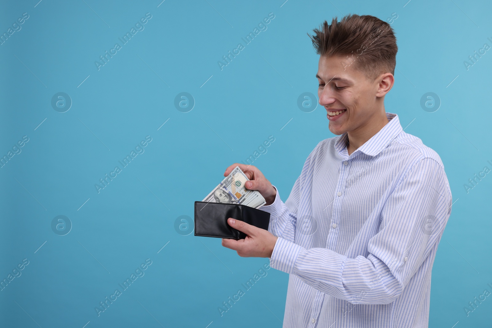 Photo of Happy man putting dollar banknotes into wallet on light blue background. Space for text