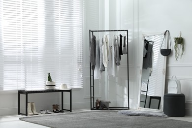 Rack with stylish women's clothes and large mirror in dressing room. Interior design