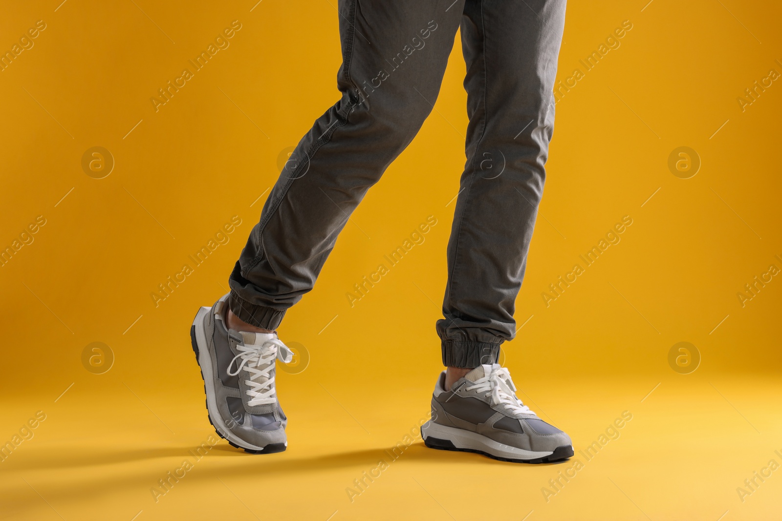 Photo of Man walking in sneakers on yellow background, closeup