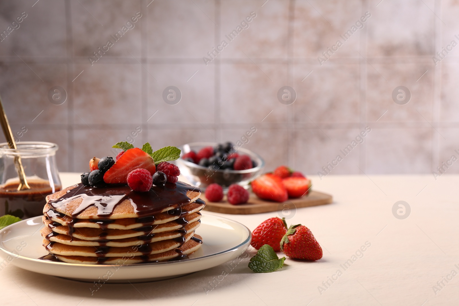 Photo of Stack of tasty pancakes with fresh berries, chocolate sauce and mint on white table. Space for text