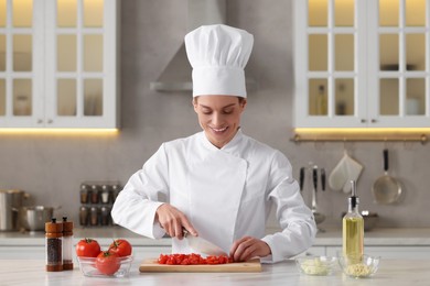 Photo of Professional chef cutting tomatoes at white marble table indoors