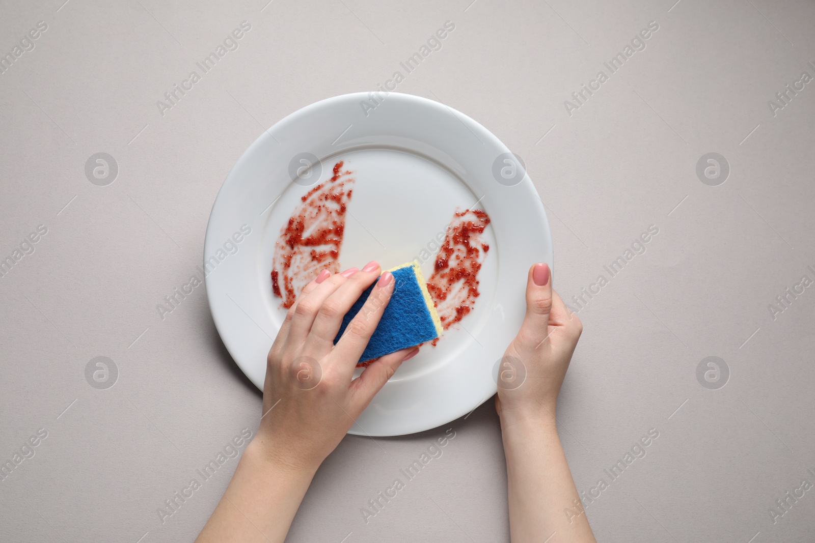 Photo of Woman washing dirty plate with sponge on light grey background, top view