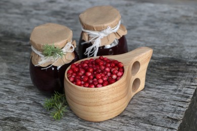 Photo of Tasty lingonberry jam in jars and cup with red berries on wooden table