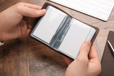 Man holding leather business card holder with blank cards at wooden table, closeup