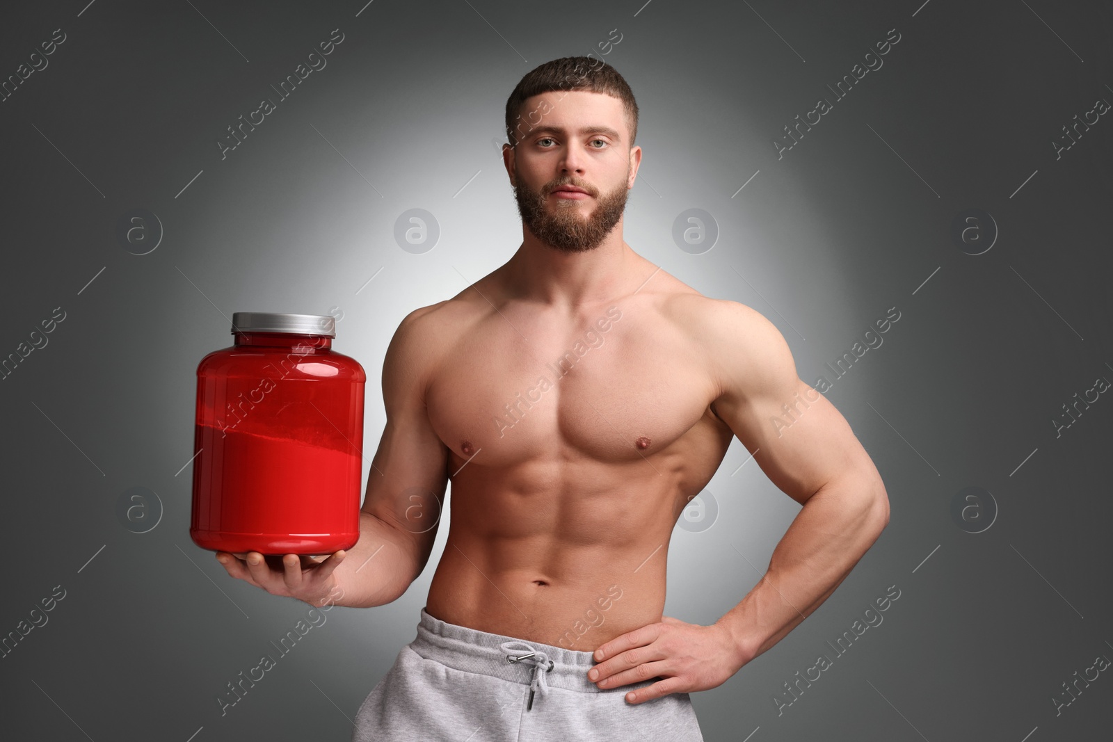 Photo of Young man with muscular body holding jar of protein powder on grey background