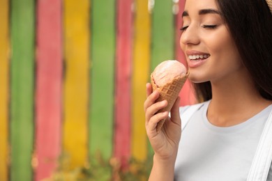 Photo of Happy young woman with delicious ice cream in waffle cone outdoors. Space for text