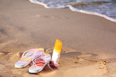 Photo of Flip flops and beach accessories on sand near sea. Space for text
