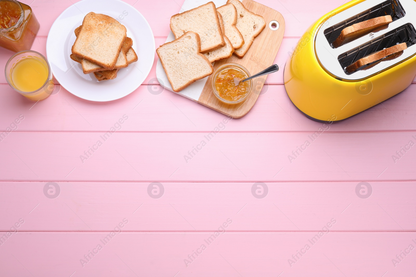 Photo of Yellow toaster with roasted bread, glass of juice and jam on pink wooden table, flat lay. Space for text