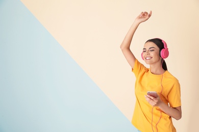 Photo of Attractive woman with mobile phone enjoying music in headphones on color background. Space for text