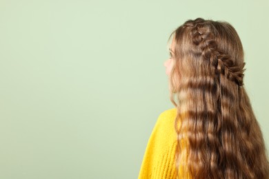 Cute little girl with braided hair on light green background. Space for text
