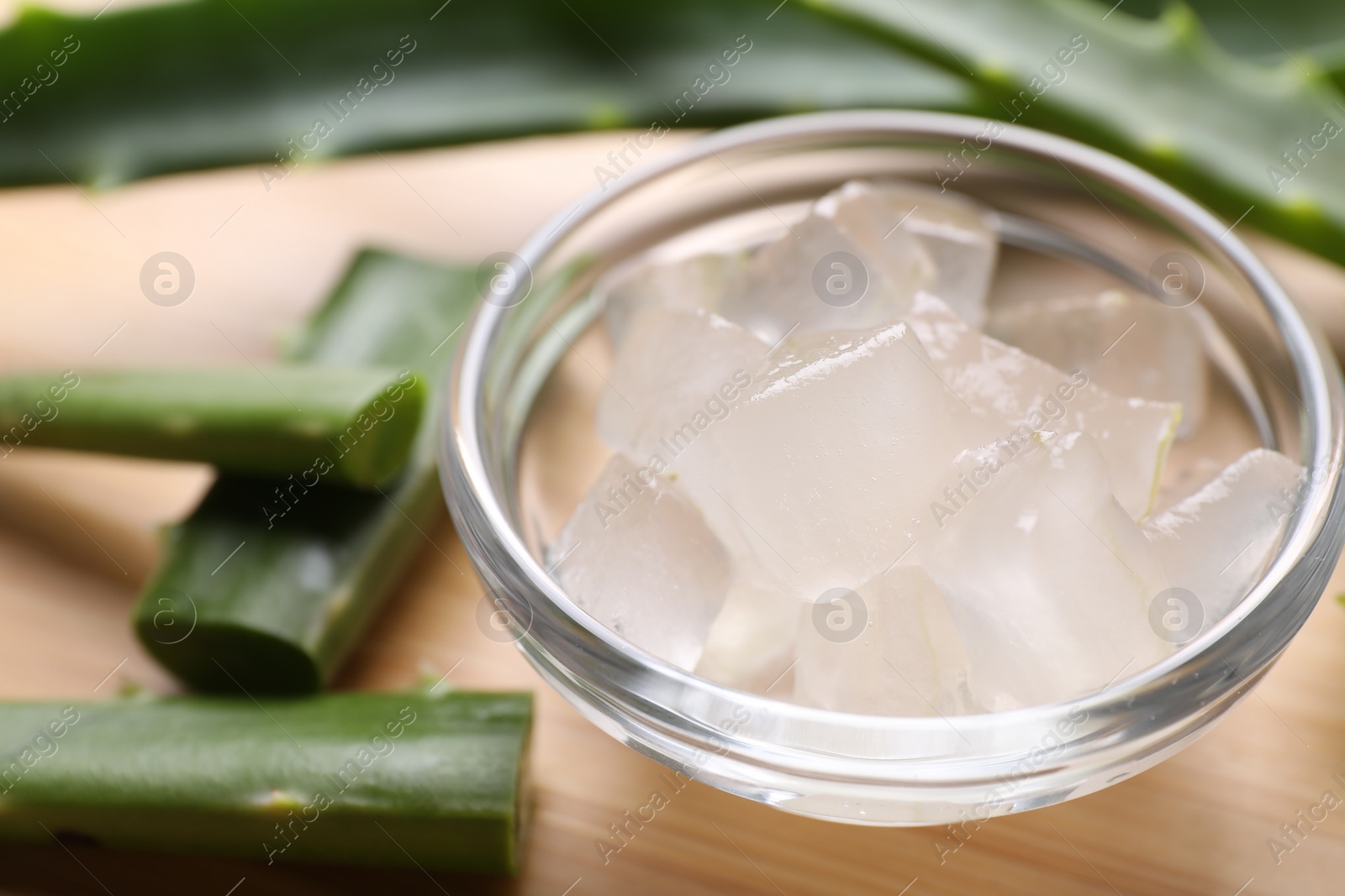 Photo of Aloe vera gel and slices of plant on wooden table, closeup