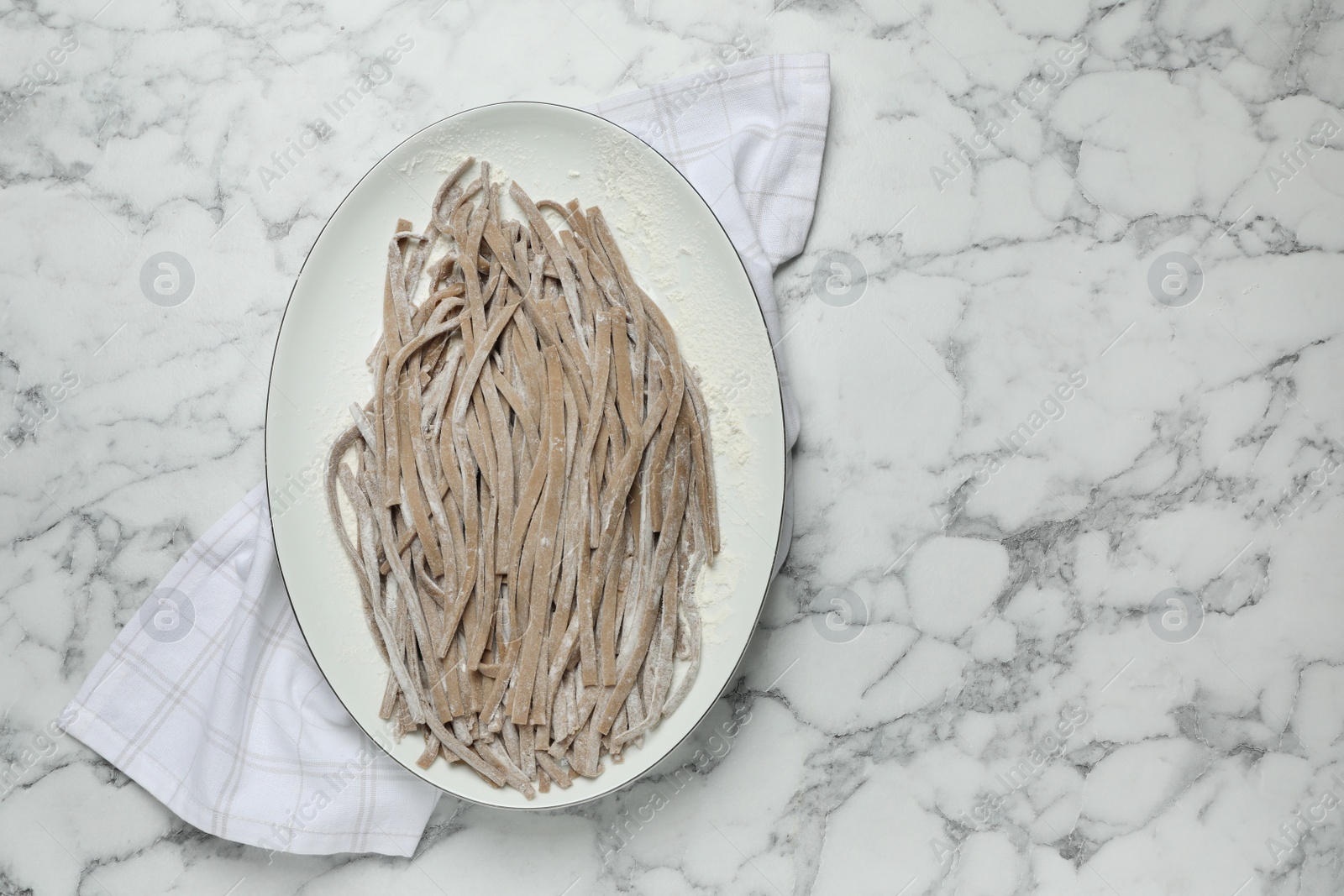 Photo of Uncooked homemade soba (buckwheat noodles) and napkin on white marble table, top view. Space for text