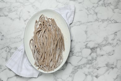 Uncooked homemade soba (buckwheat noodles) and napkin on white marble table, top view. Space for text