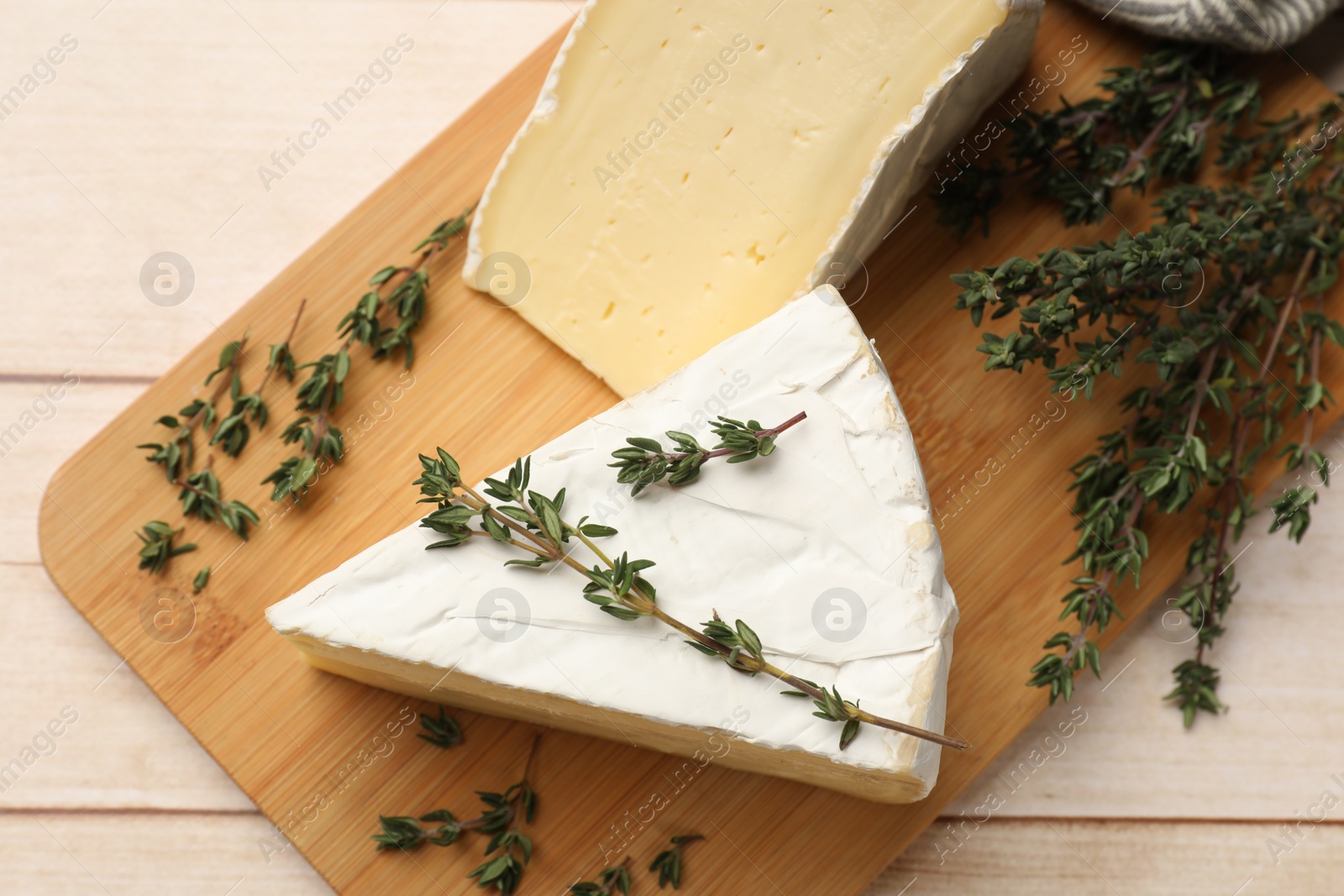 Photo of Board with pieces of tasty camembert cheese and thyme on light wooden table, top view