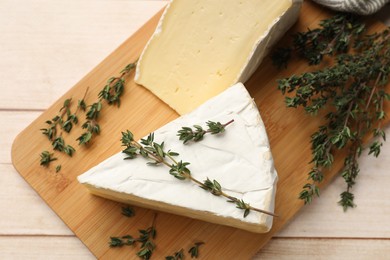 Board with pieces of tasty camembert cheese and thyme on light wooden table, top view