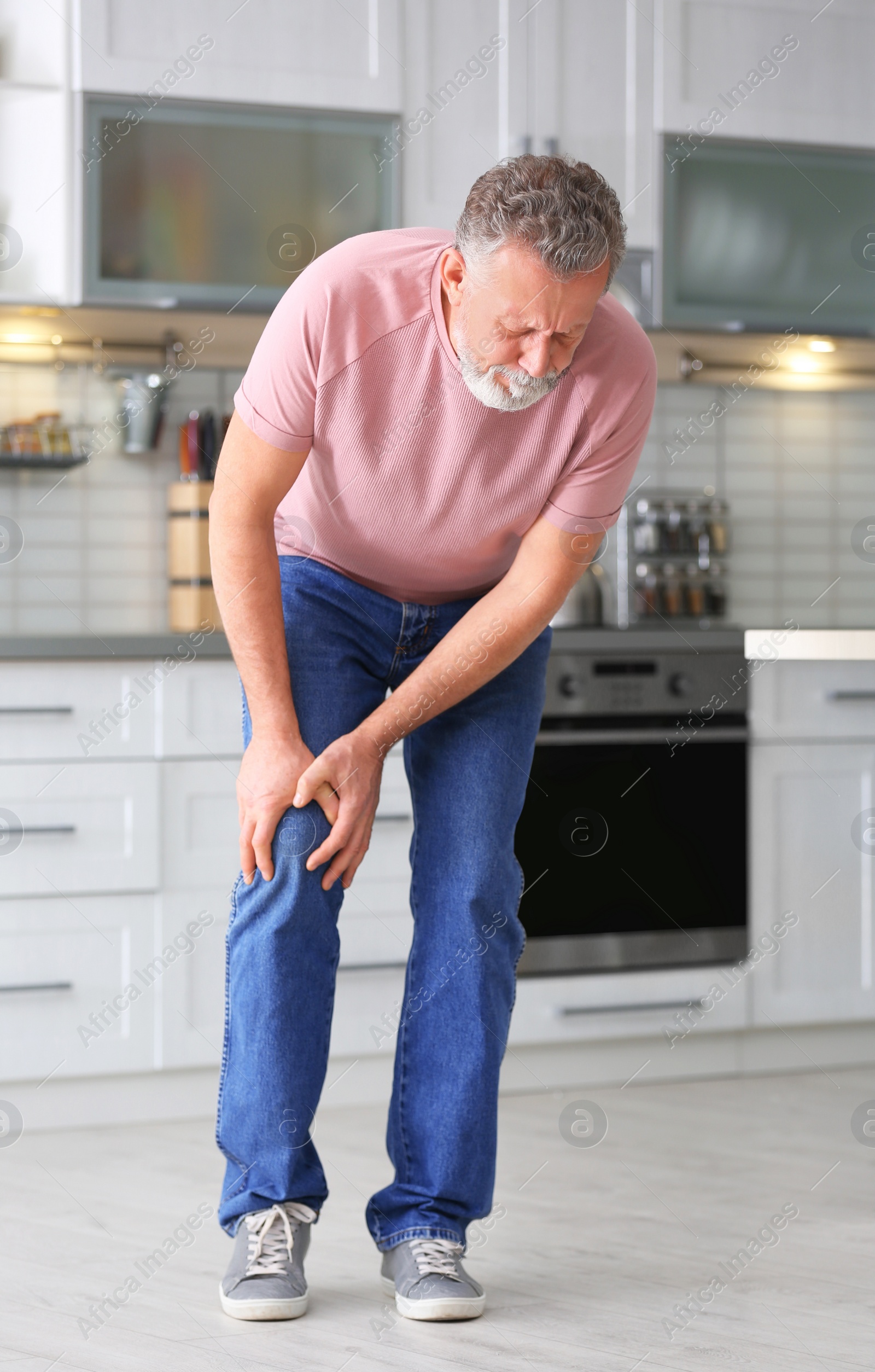 Photo of Senior man suffering from knee pain in kitchen
