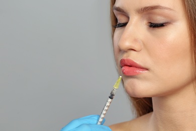 Young woman getting lips injection on grey background, space for text. Cosmetic surgery