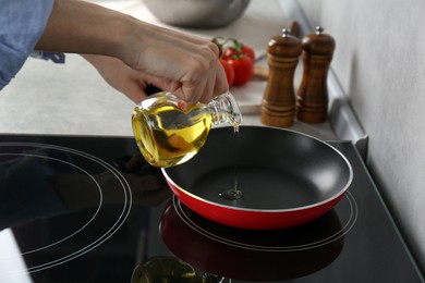 Vegetable fats. Woman pouring cooking oil into frying pan on stove in kitchen, closeup
