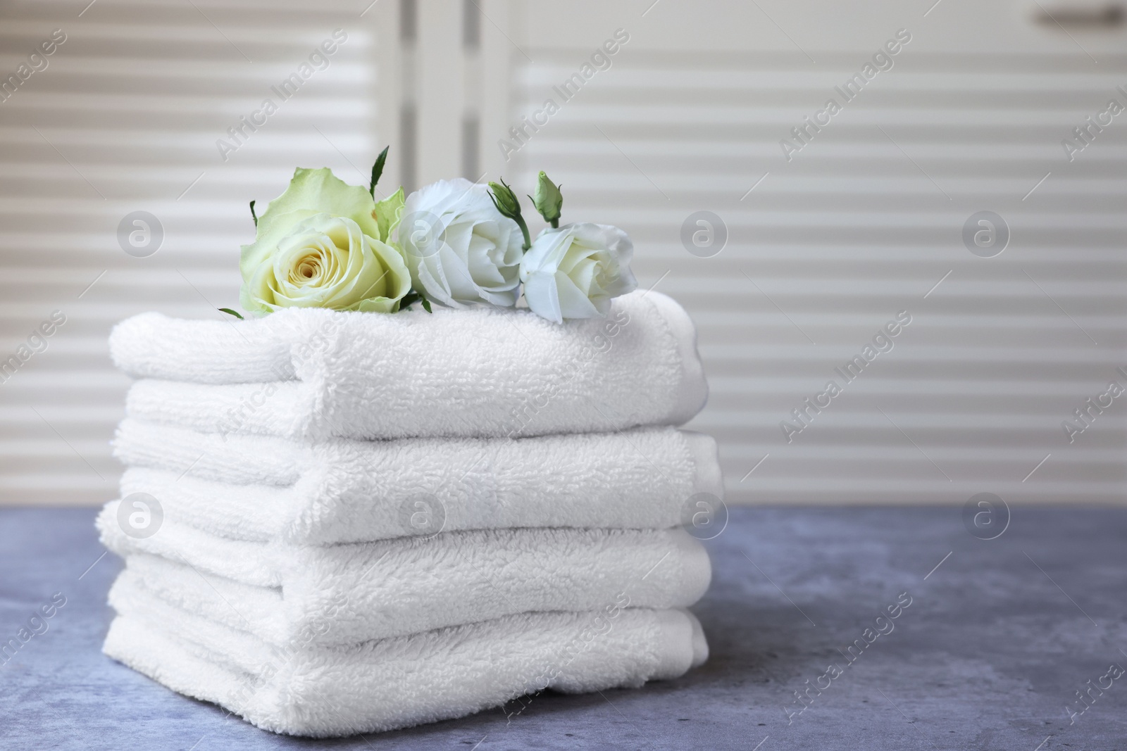 Photo of Folded towels with flowers on grey table indoors, space for text