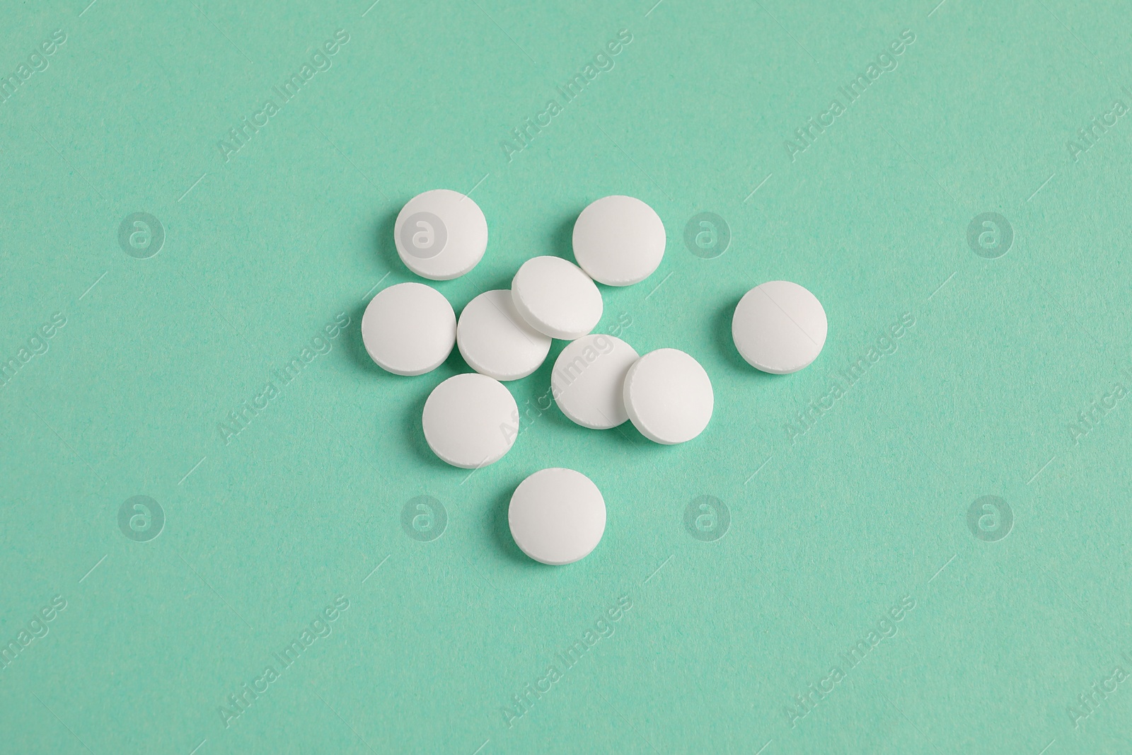 Photo of Pile of white pills on green background, flat lay