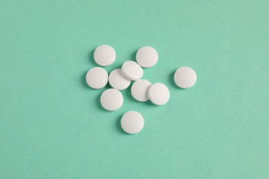 Photo of Pile of white pills on green background, flat lay