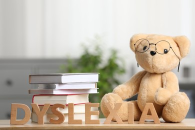 Photo of Teddy bear in glasses, books and word Dyslexia made of letters on wooden table indoors