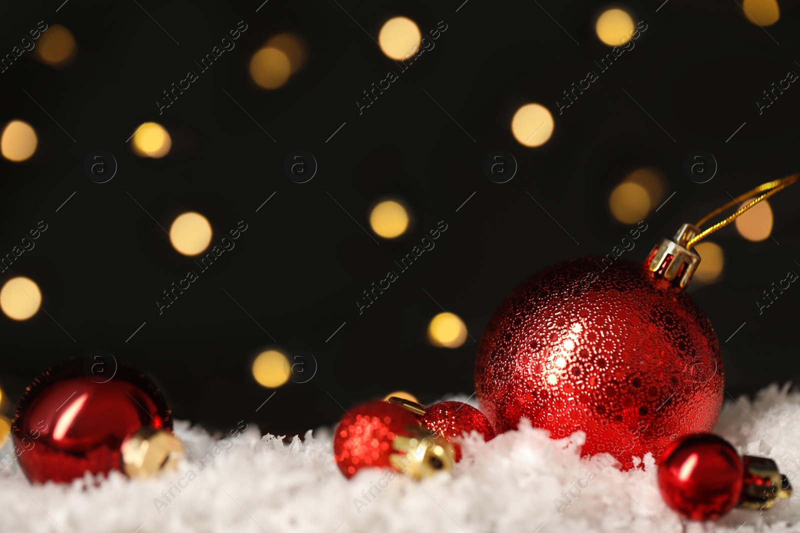 Photo of Beautiful Christmas balls on snow against blurred festive lights. Space for text