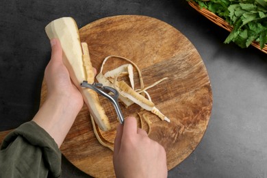 Photo of Woman peeling fresh ripe parsnip at black table, above view