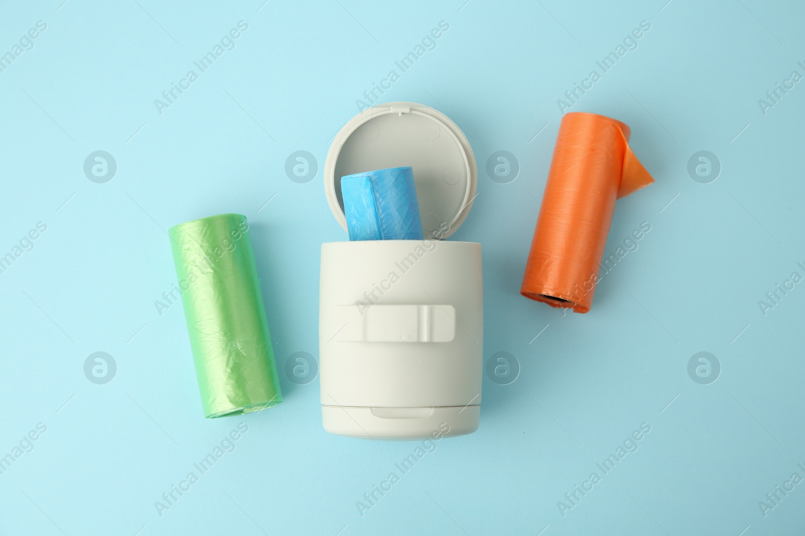 Photo of Dog waste bags and dispenser on light blue background, flat lay