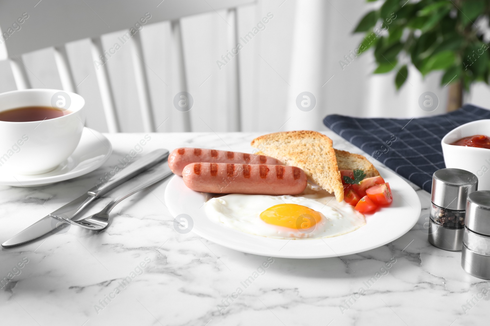 Photo of Tasty breakfast with fried egg and sausages served on white marble table indoors