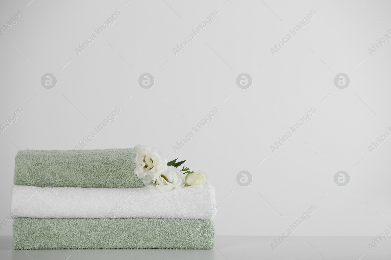 Photo of Soft folded towels with eustoma flowers on white table, space for text