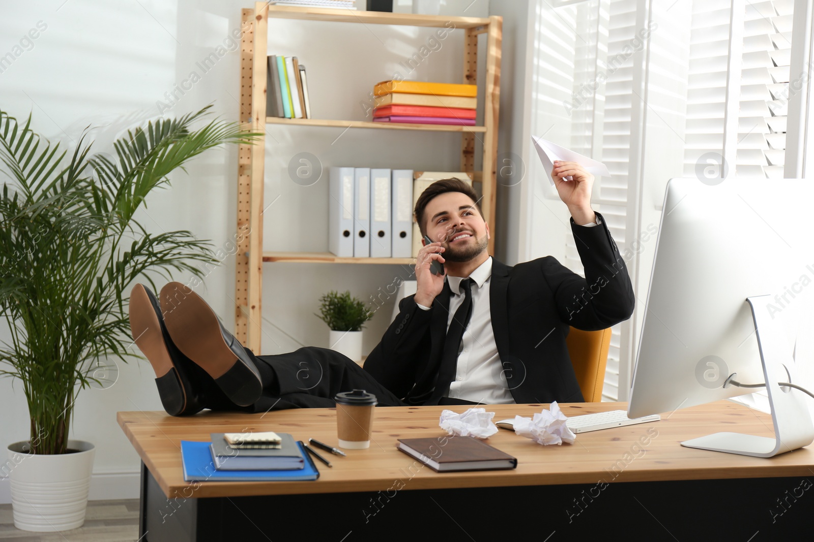 Photo of Lazy employee playing with paper plane at table in office