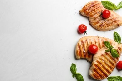 Photo of Tasty grilled chicken fillets with cherry tomatoes and green basil on light grey table, flat lay. Space for text