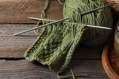 Photo of Soft green woolen yarn, knitting and needles on wooden table, closeup