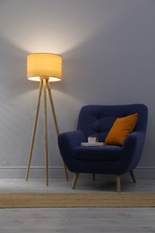 Photo of Stylish tripod floor lamp near blue armchair indoors. Interior design