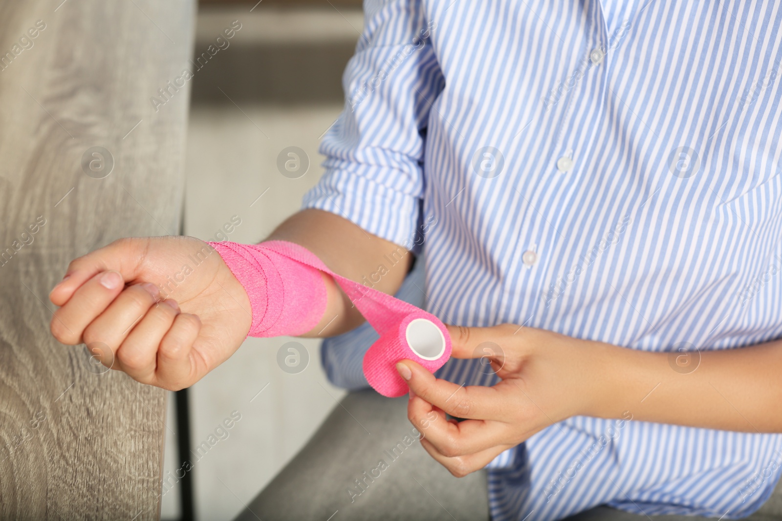 Photo of Young woman applying medical bandage onto wrist in office, closeup